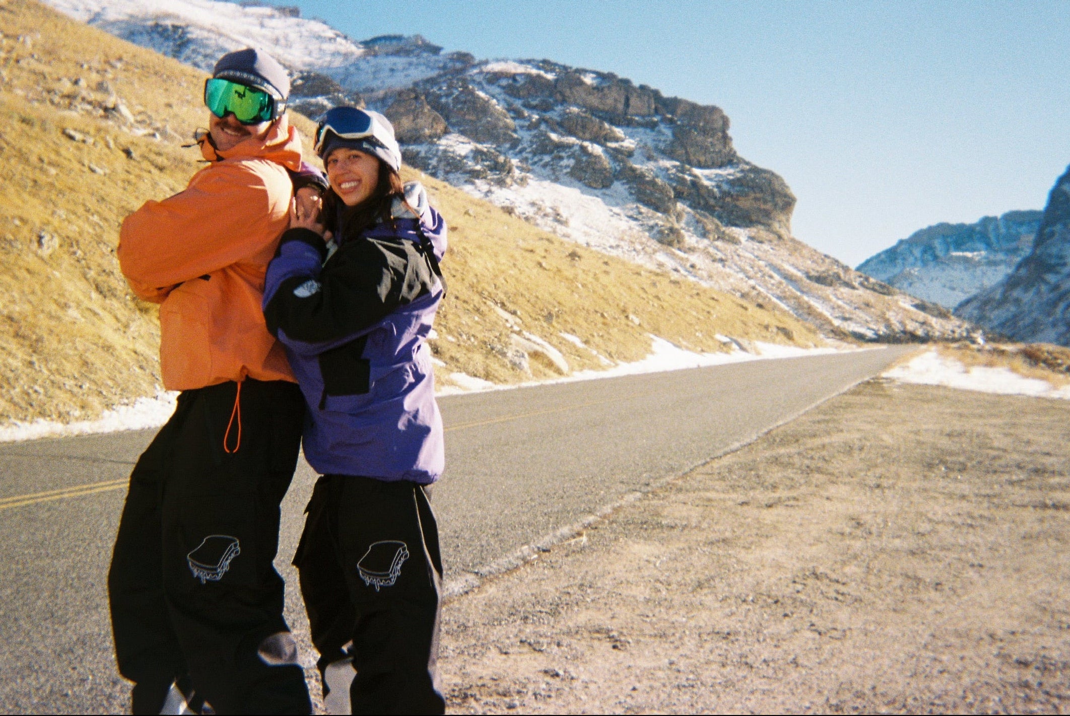 Two people posing on a road with mountains in the background